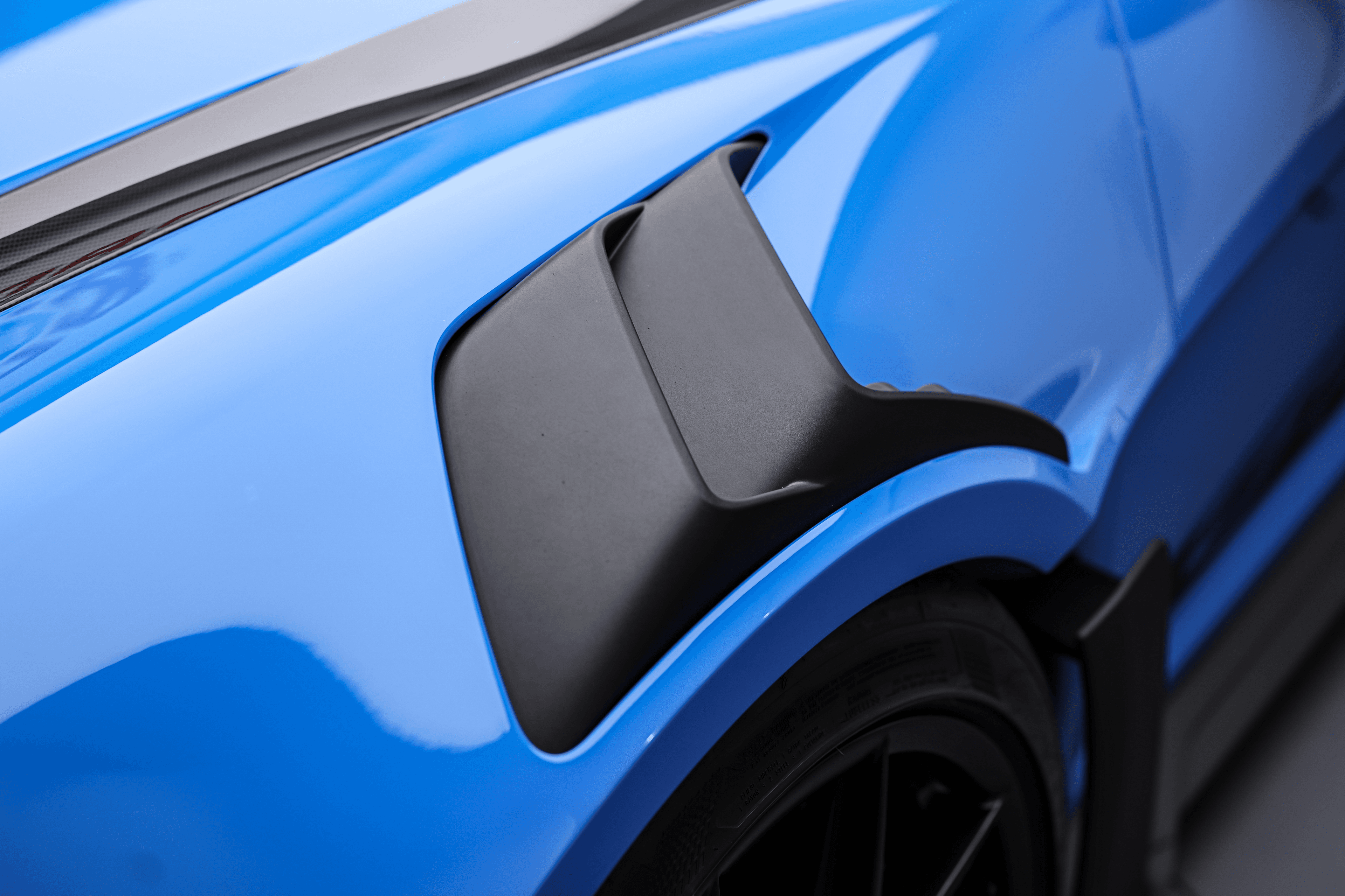 Zoom sur le détail du passage d'air de la Porsche GT3RS shark blue, conçu pour améliorer le refroidissement et l'aérodynamisme, crucial pour des performances de pointe.