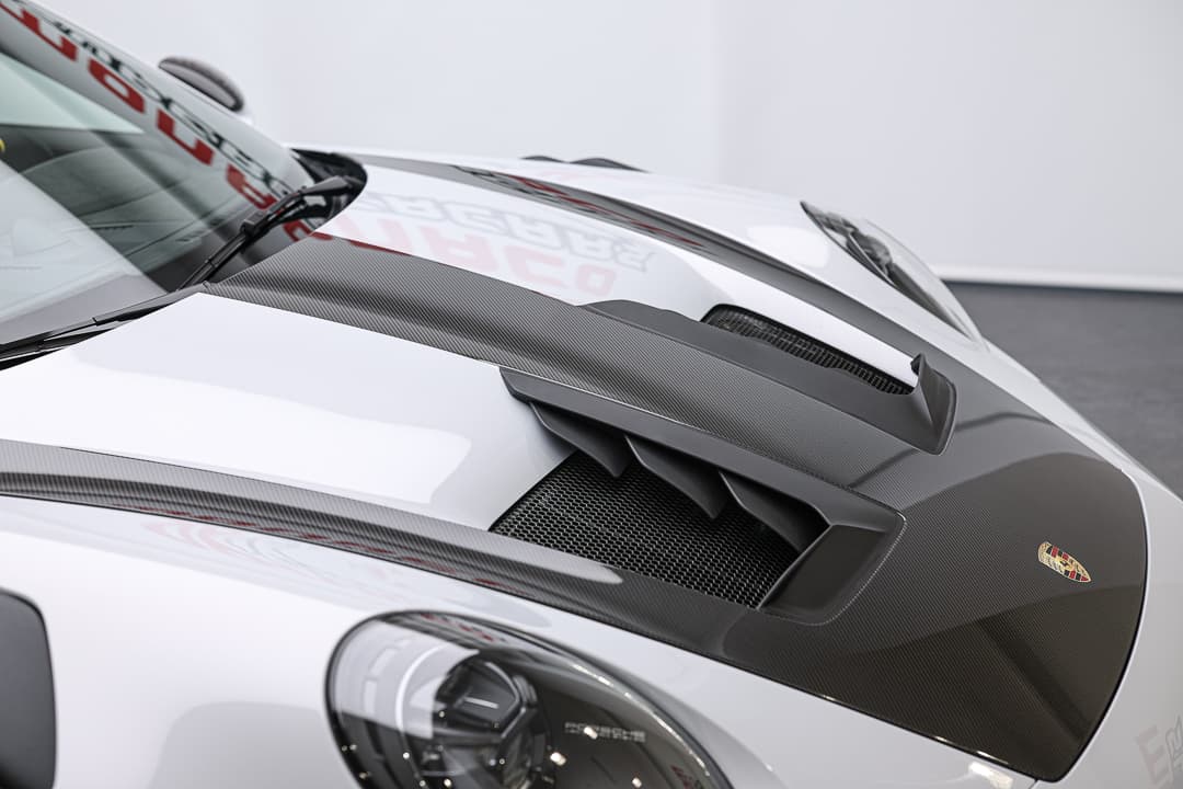 Cette vue du capot en carbone de la Porsche 911 GT3 RS met en avant son design léger et robuste, soulignant non seulement l'esthétique sportive, mais aussi l'engagement de la marque pour la performance et l'efficacité aérodynamique.