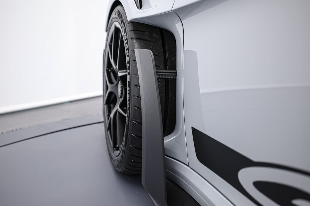 Cette image illustre l'aérodynamique avancée de la Porsche 911 GT3 RS, mettant en évidence des éléments tels que le spoiler avant et les prises d'air stratégiquement placées, conçus pour maximiser la performance et la stabilité à des vitesses élevées.