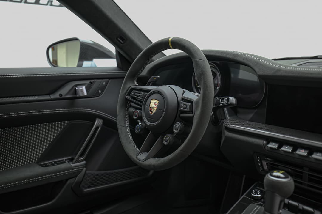 Cette vue éloignée du tableau de bord de la Porsche 911 GT3 RS offre une perspective globale sur le cockpit, mettant en avant l'harmonie entre les éléments de design, la disposition des instruments et l'ambiance sportive, tout en soulignant l'ergonomie dédiée à l'expérience de conduite.