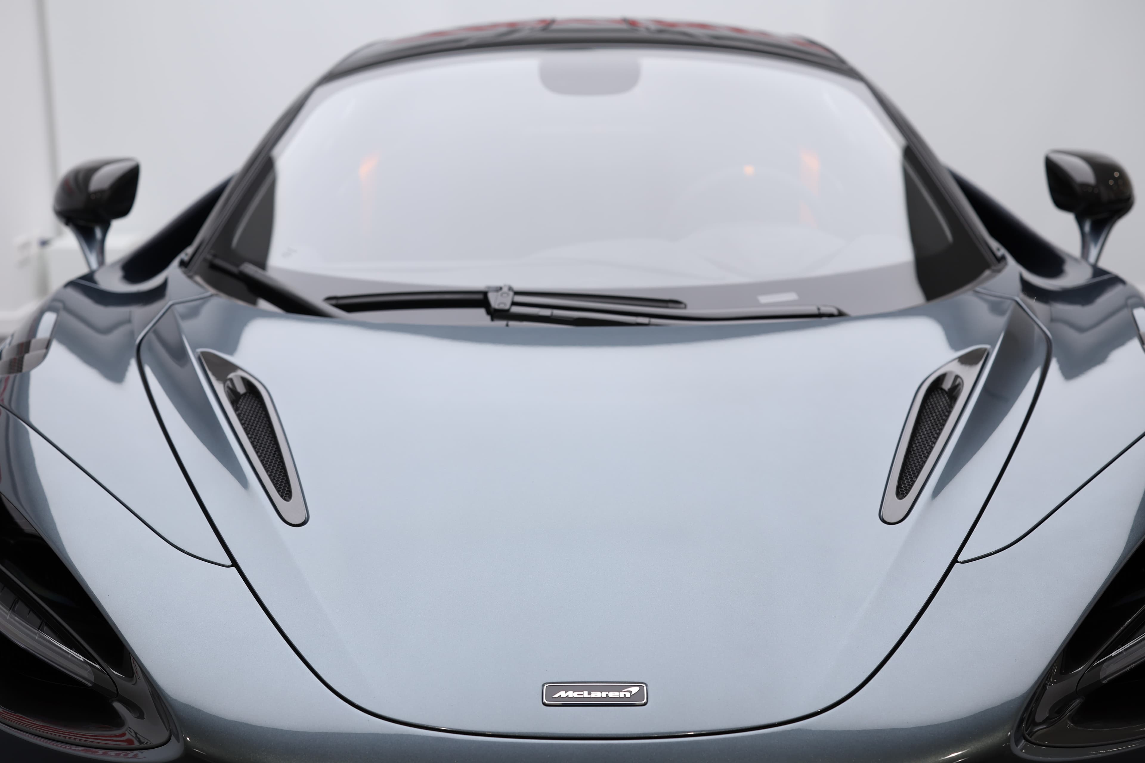 L'image montre le capot d'une McLaren 765LT, mettant en avant ses lignes sculptées et aérodynamiques, ainsi que les évents de ventilation qui soulignent la performance et l'ingénierie avancée de la voiture.