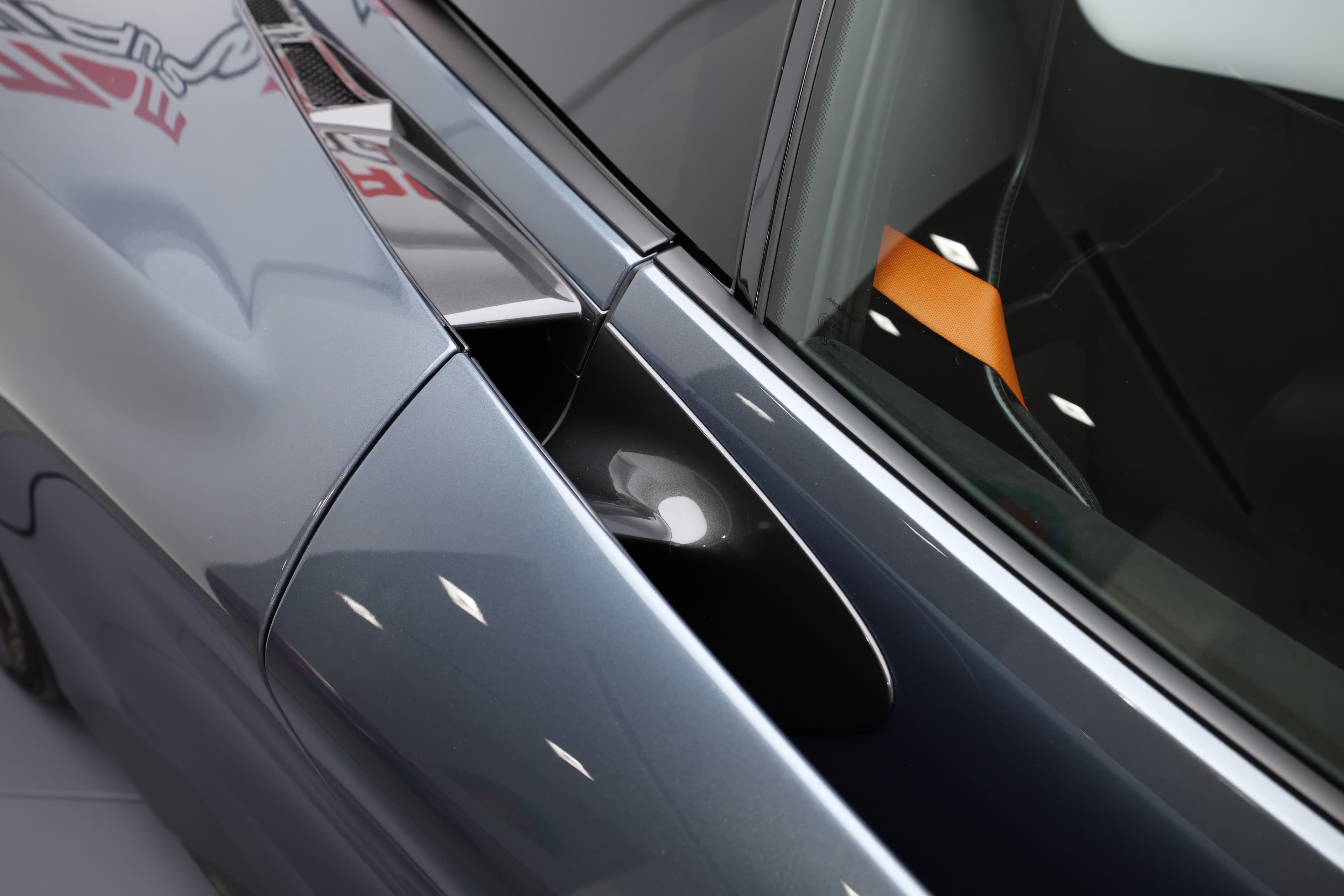 L'image montre la moitié avant de profil de la McLaren 765LT, mettant en avant ses lignes aérodynamiques, son capot sculpté et ses phares distinctifs, qui soulignent le caractère sportif et agressif de la voiture.