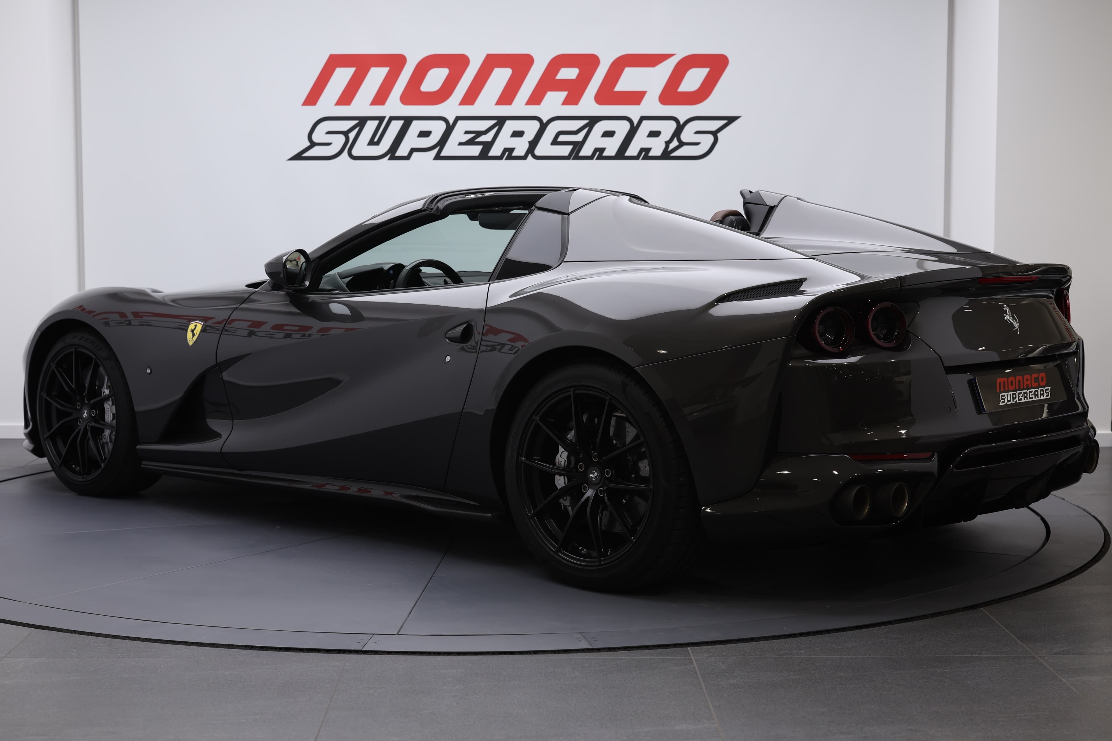 La photo montre une Ferrari 812 GTS vue de trois quarts arrière, avec le toit décapoté, mettant en valeur son design aérodynamique et la puissance qui s'en dégage.