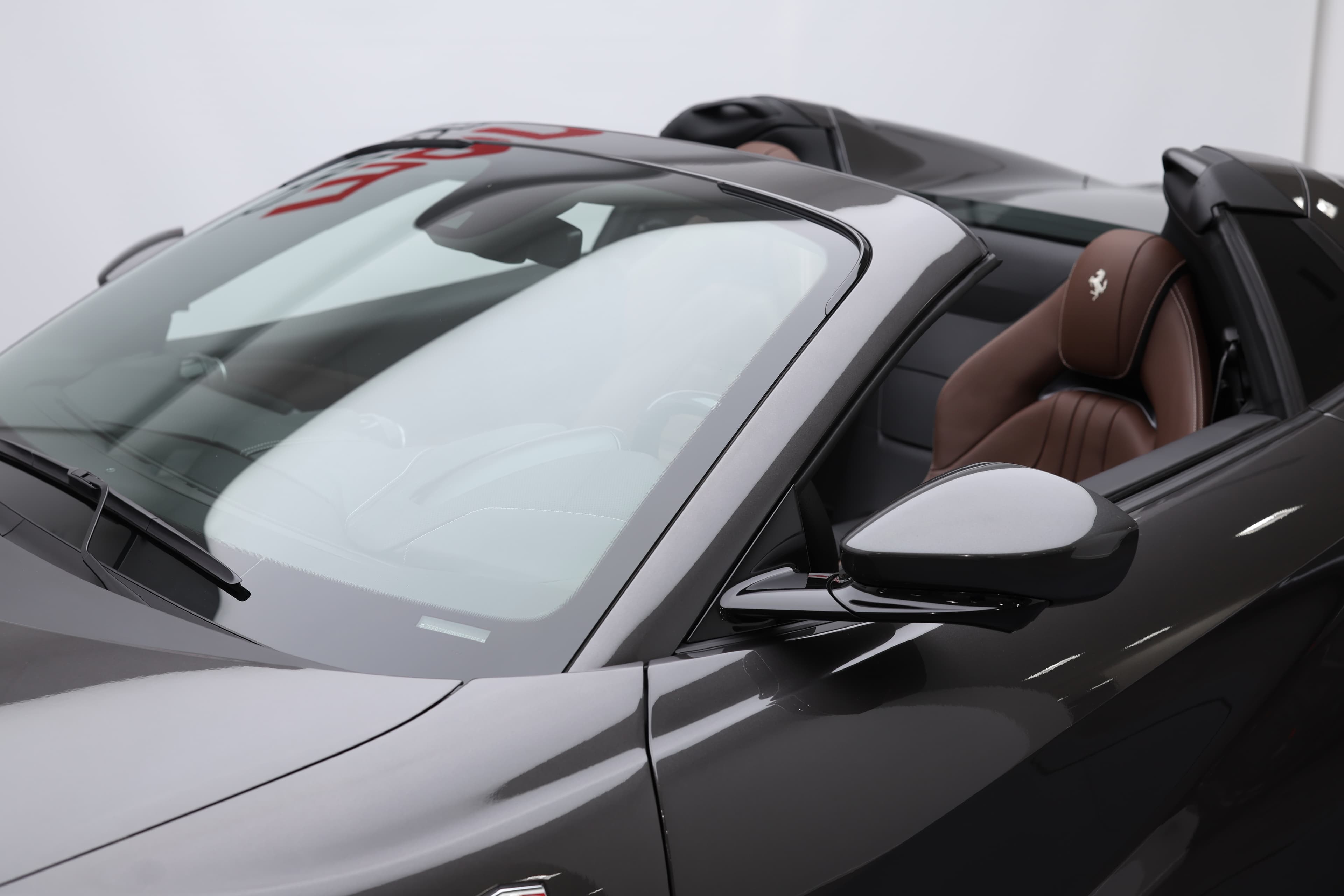 La photo montre le pare-brise de la Ferrari 812 GTS décapotée, révélant un intérieur en cuir chocolat qui allie luxe et sportivité, créant une ambiance chaleureuse et raffinée.