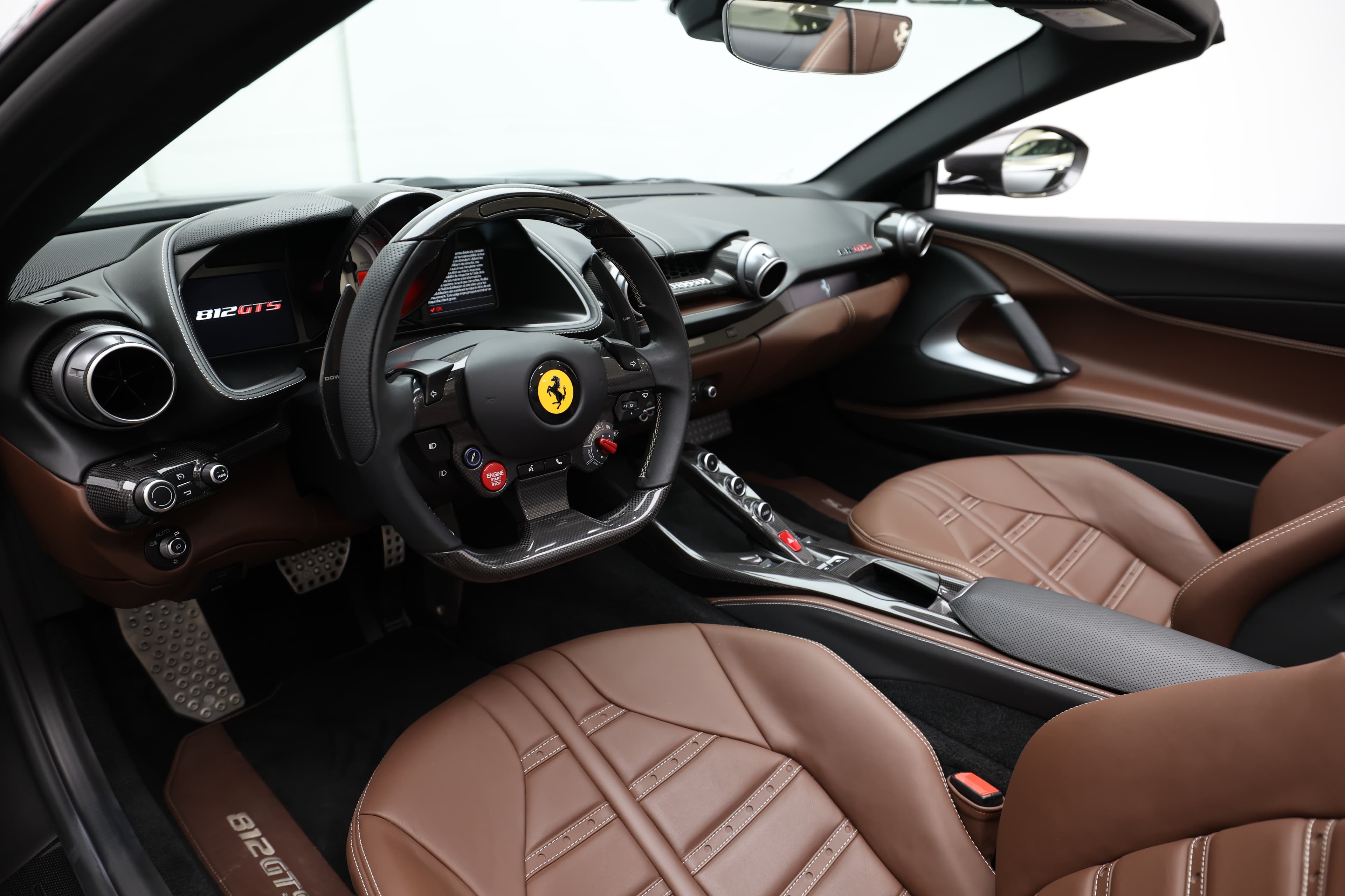 Voici une vue d'ensemble de l'intérieur de la Ferrari 812 GTS, mettant en avant le volant emblématique et les sièges en cuir chocolat. Le design sportif et ergonomique, associé aux matériaux haut de gamme, crée une ambiance à la fois luxueuse et orientée vers la performance.