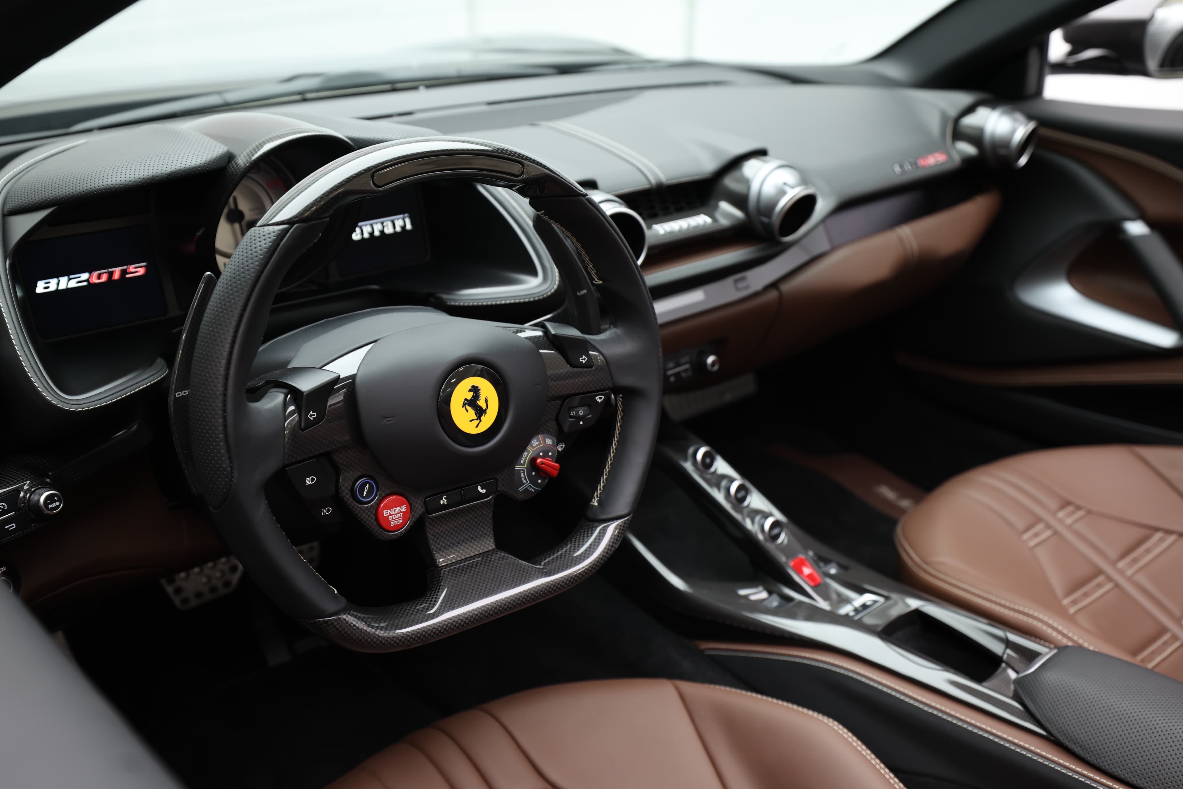 Voici une vue d'ensemble de l'intérieur de la Ferrari 812 GTS, mettant en avant le volant et la console centrale. Le cuir chocolat et les finitions en métal créent une atmosphère luxueuse, tandis que le design sportif souligne l'ADN de performance de cette supercar.