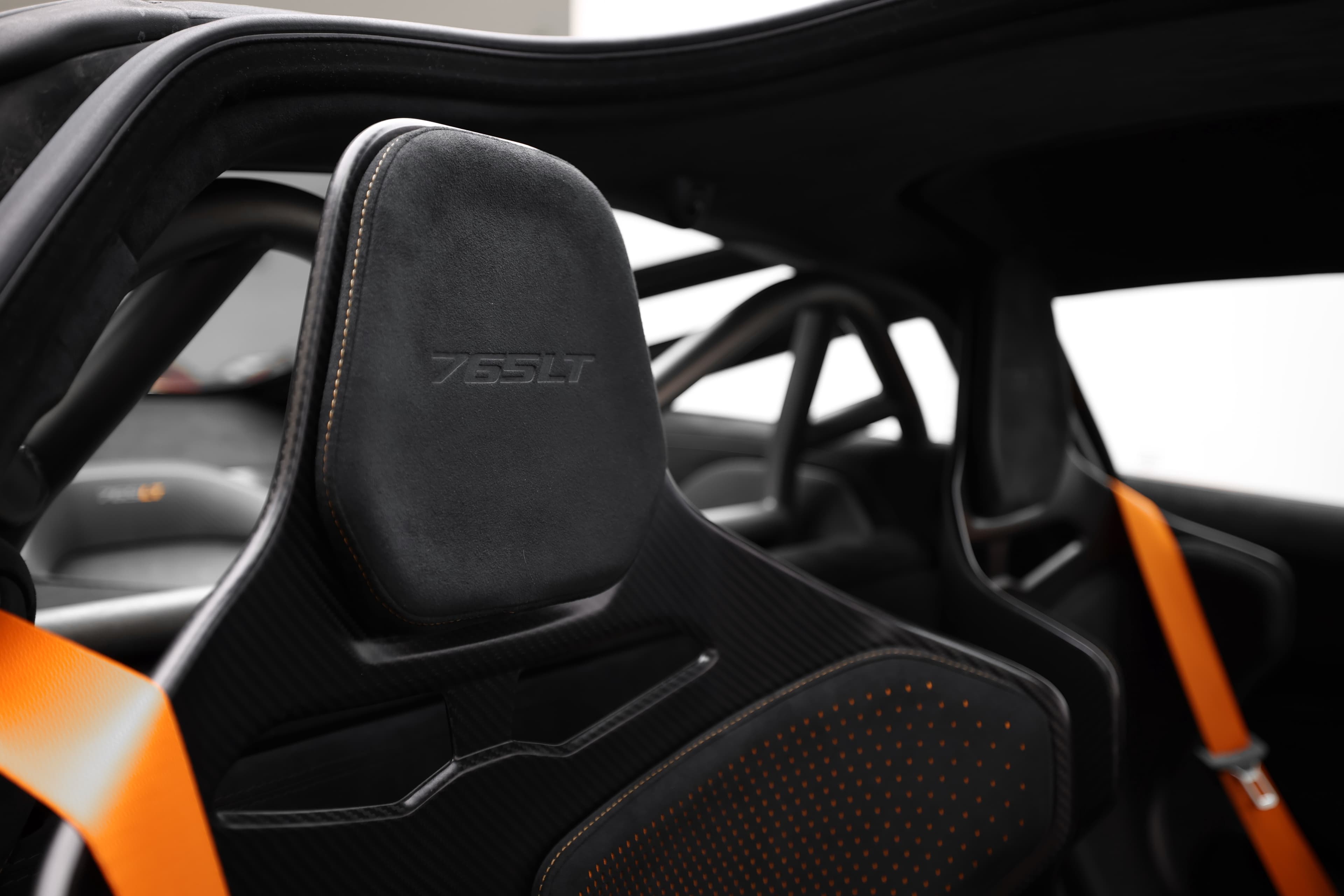 Gros plan sur le siège de la McLaren 765LT, mettant en avant le logo 765LT brodé, les harnais de sécurité et la conception axée sur le soutien, soulignant l'orientation vers la performance et la sécurité.