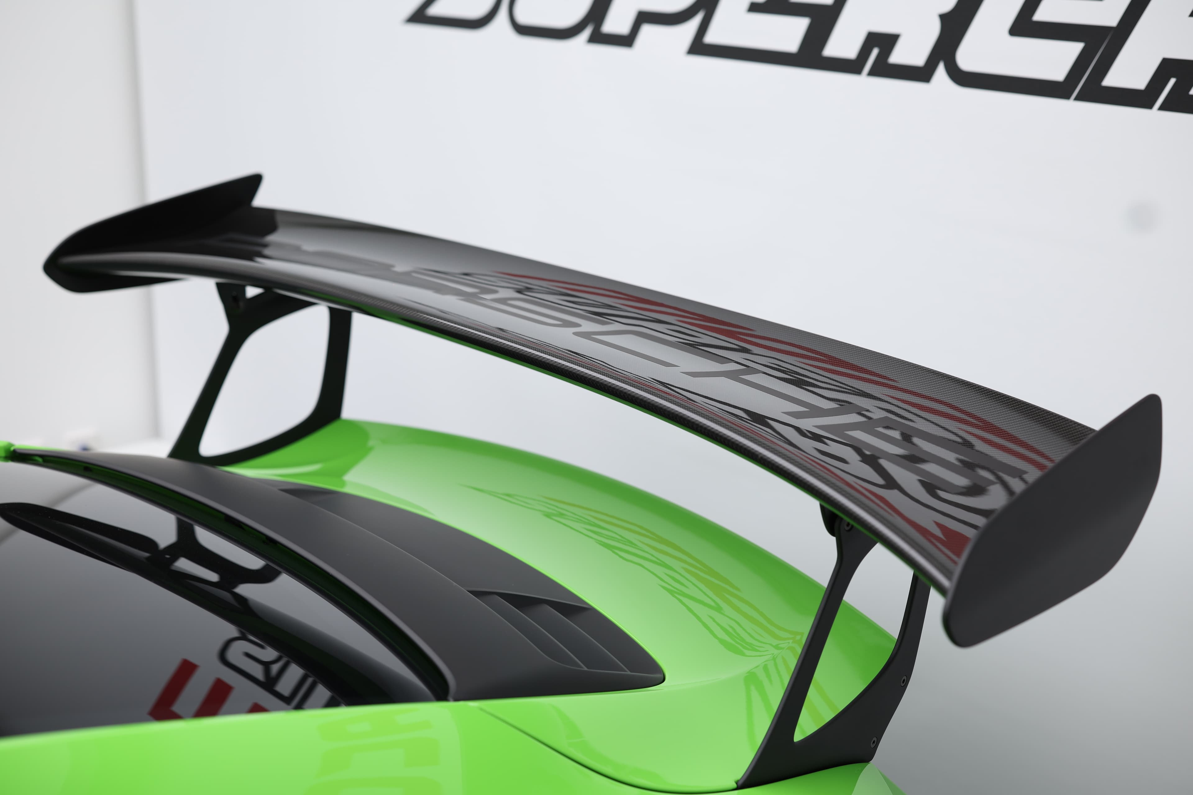 Détail de l’aileron arrière en carbone de la Porsche 911 GT3 RS 991 verte, élément aérodynamique emblématique assurant un appui maximal pour une performance optimale sur circuit.