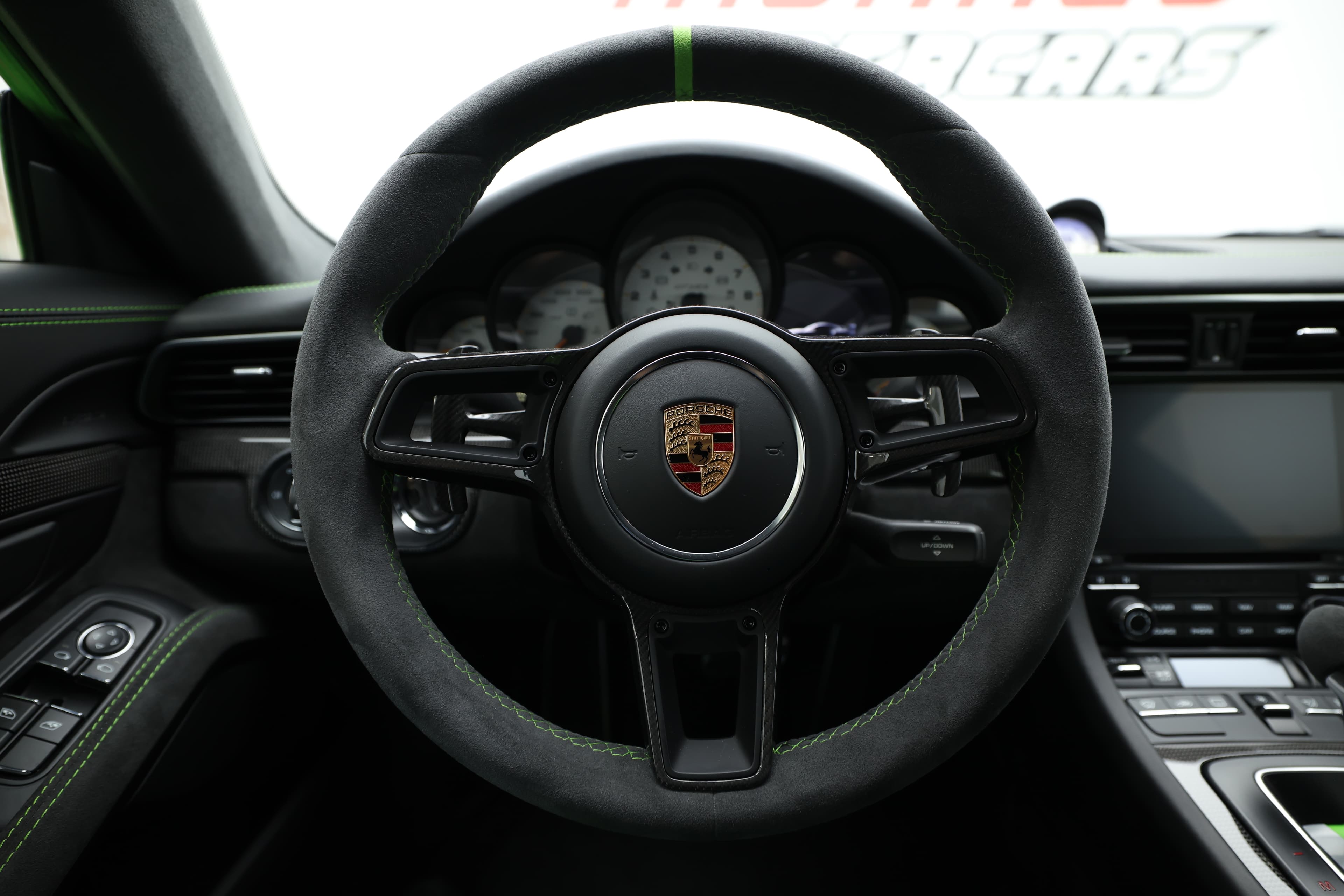 Le volant de la Porsche GT3 RS, recouvert d'Alcantara et avec le logo emblématique au centre, offre une prise en main optimale pour une conduite sportive. Le design épuré et les touches de vert ajoutent une note d'agressivité à l'ensemble.