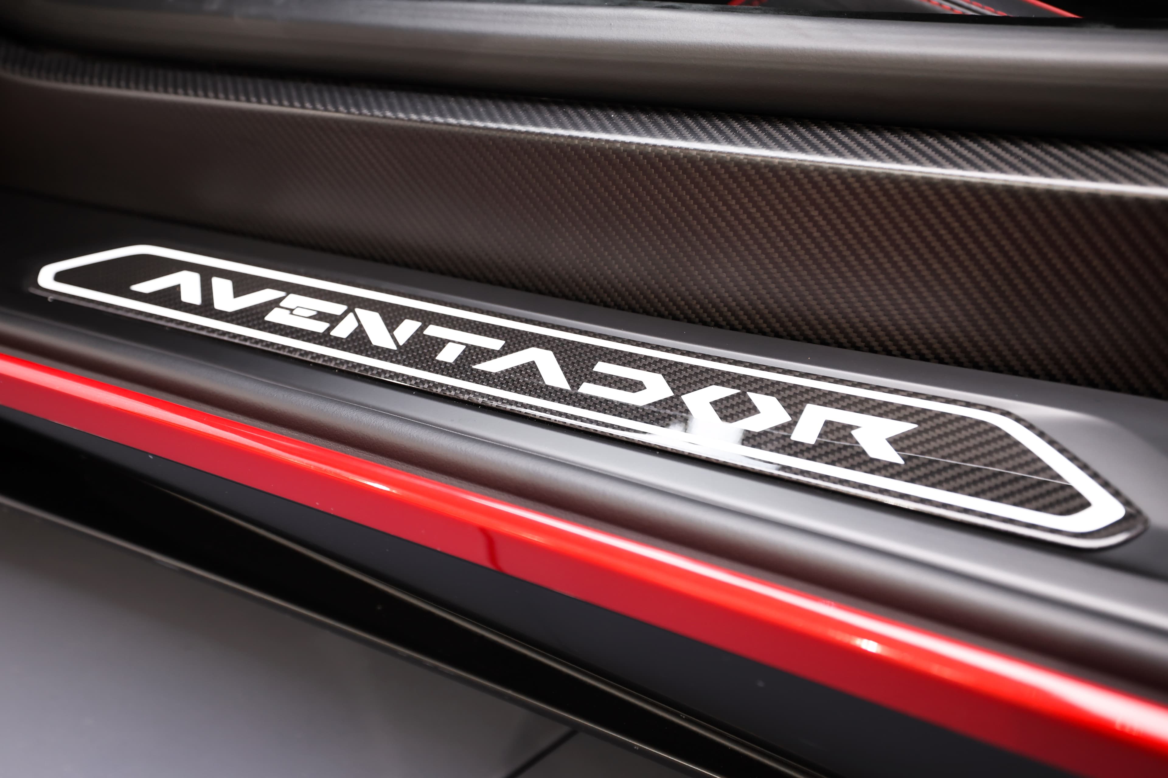 Zoom sur le badge 'Aventador SV' à l'intérieur de la Lamborghini, une touche distinctive qui souligne l'héritage et la puissance de ce modèle emblématique, tout en étant intégré dans un design raffiné en carbone.