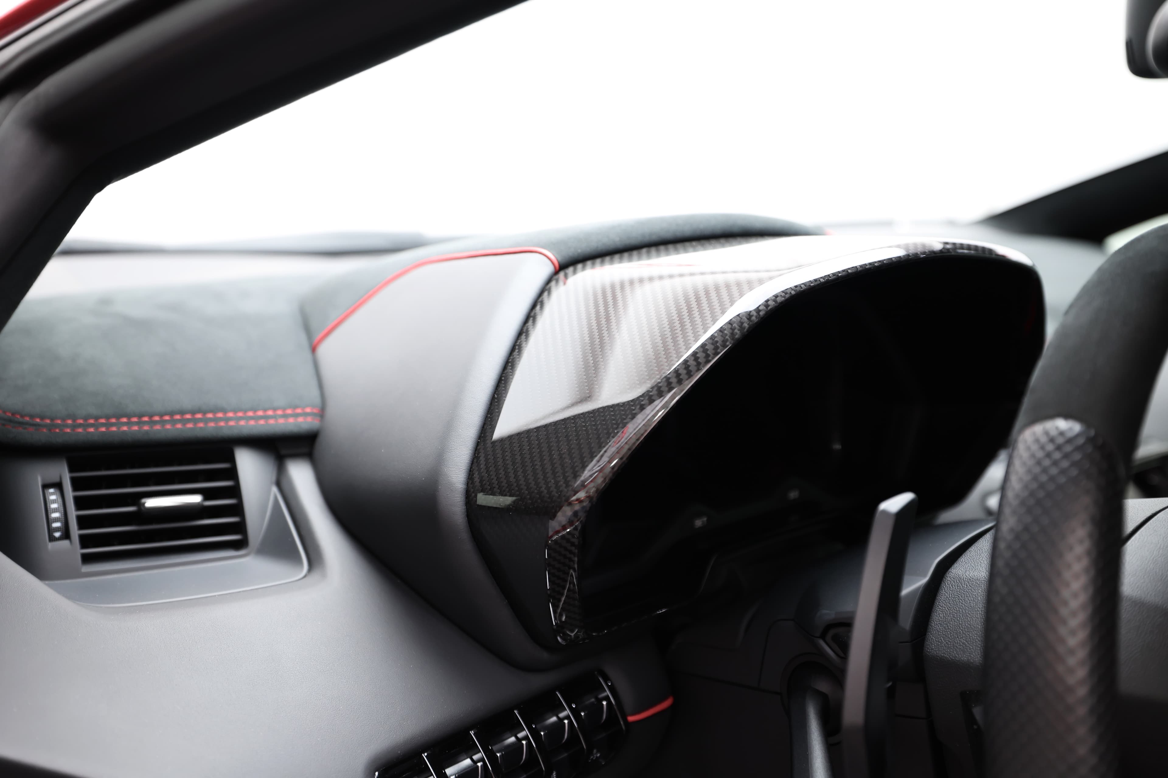 Vue rapprochée d'un détail du tableau de bord de la Lamborghini Aventador SV, mettant en avant les finitions en carbone et les coutures rouges, qui accentuent le caractère sportif et luxueux de l'habitacle. Chaque élément est conçu pour offrir à la fois esthétique et fonctionnalité.