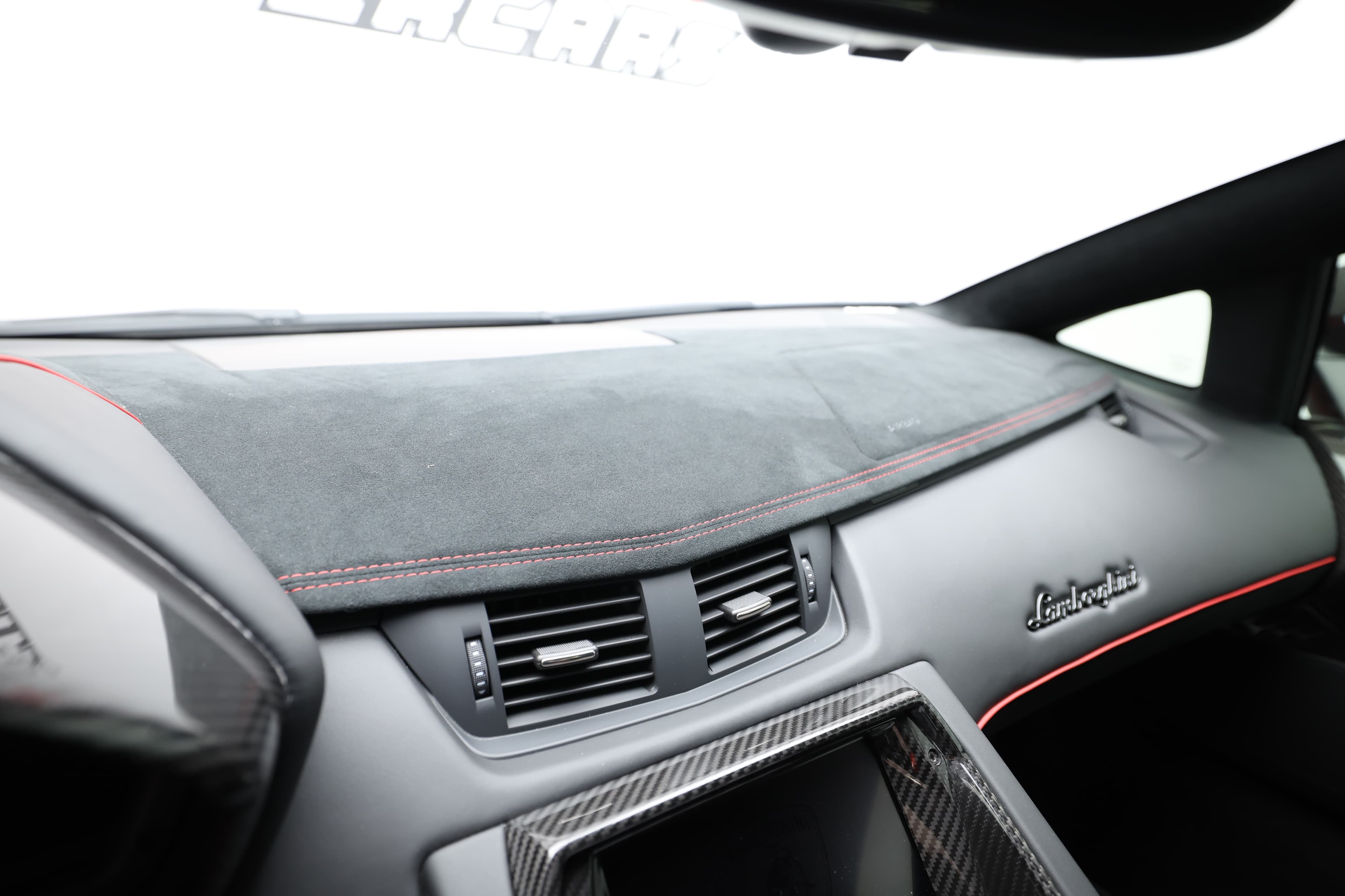 Vue panoramique du tableau de bord de la Lamborghini Aventador SV, recouvert d'une finition en alcantara. Cela renforce non seulement le luxe de l'intérieur, mais contribue également à une ambiance sportive, tout en mettant en valeur le savoir-faire artisanal de Lamborghini.