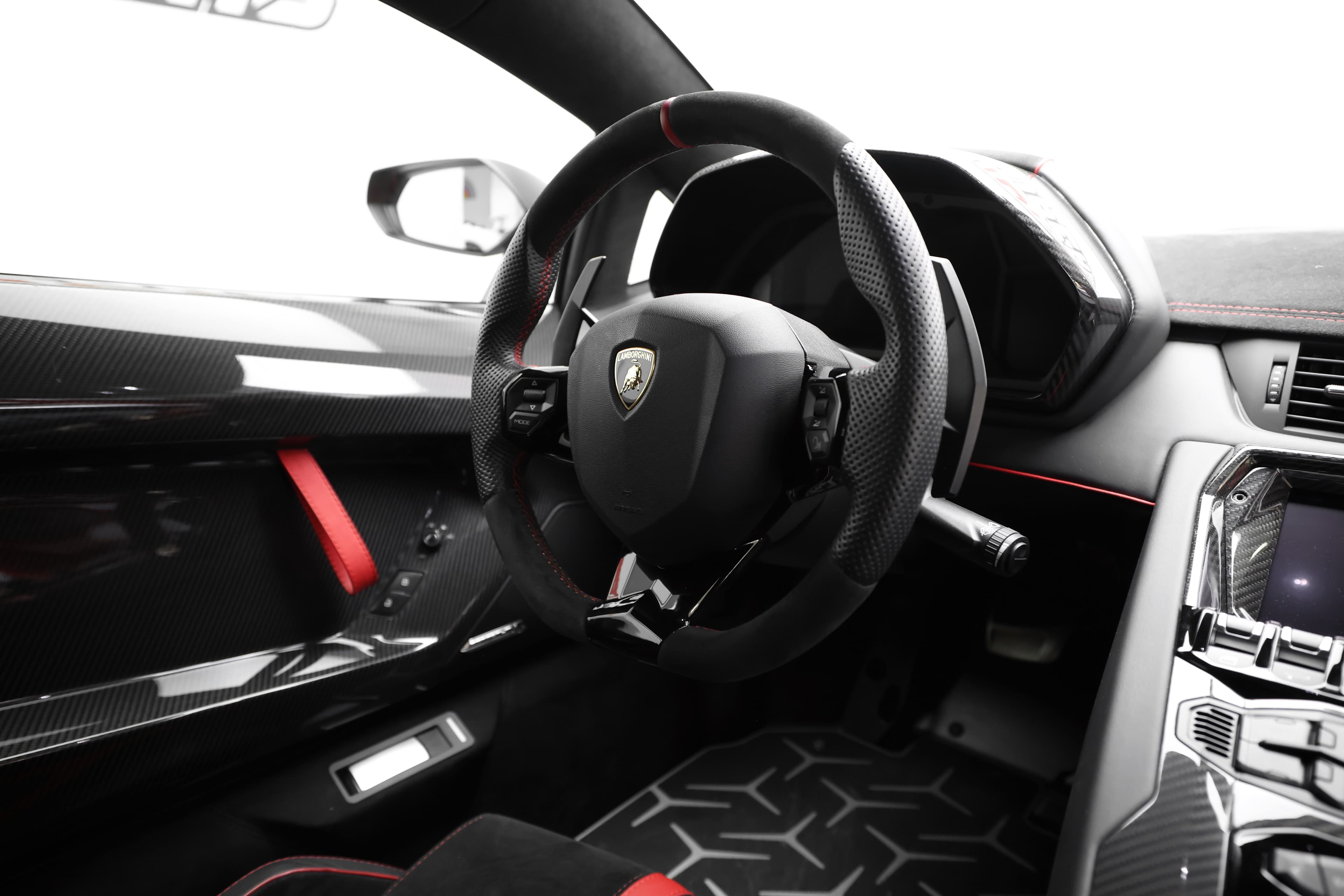 Vue rapprochée de l'intérieur de la Lamborghini, mettant en avant le volant sportif et les finitions en carbone, accentuant l'expérience de conduite dynamique.