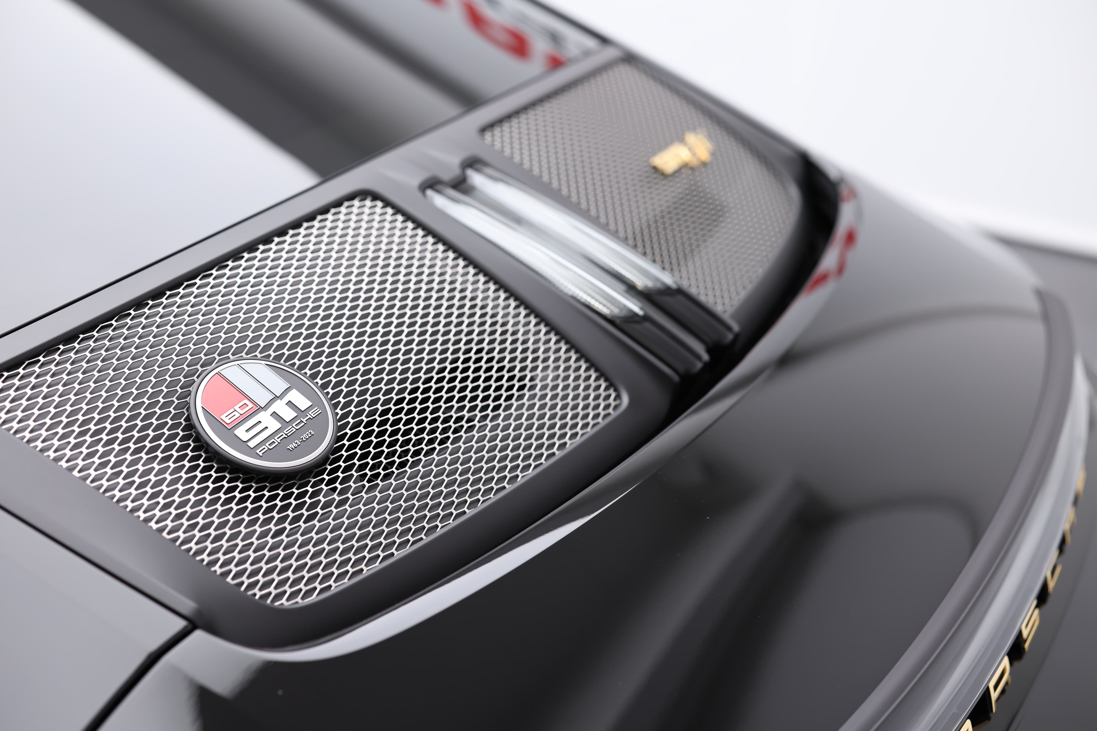 Détail du capot arrière de la Porsche 911, mettant en avant le logo "S/T" et la grille en métal, qui ajoutent une touche de sophistication tout en soulignant l'aspect sportif et performant du modèle. Ce design reflète l'héritage et l'innovation de la marque.