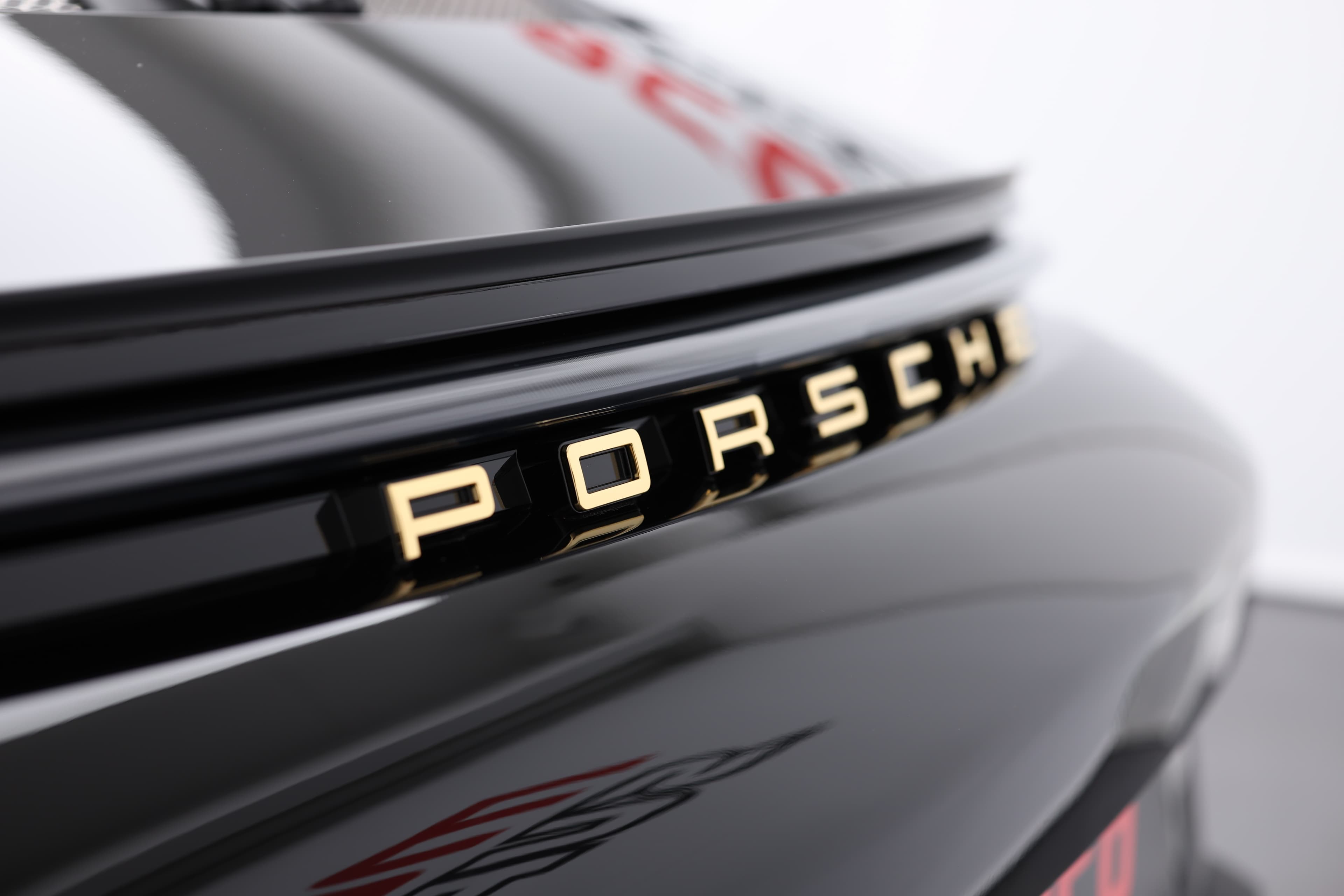 Détail du badge "PORSCHE" sur le capot arrière, mettant en valeur l'élégance du design avec une finition dorée. Ce symbole emblématique souligne non seulement la marque, mais reflète également l'héritage et l'excellence en ingénierie qui caractérisent chaque Porsche.