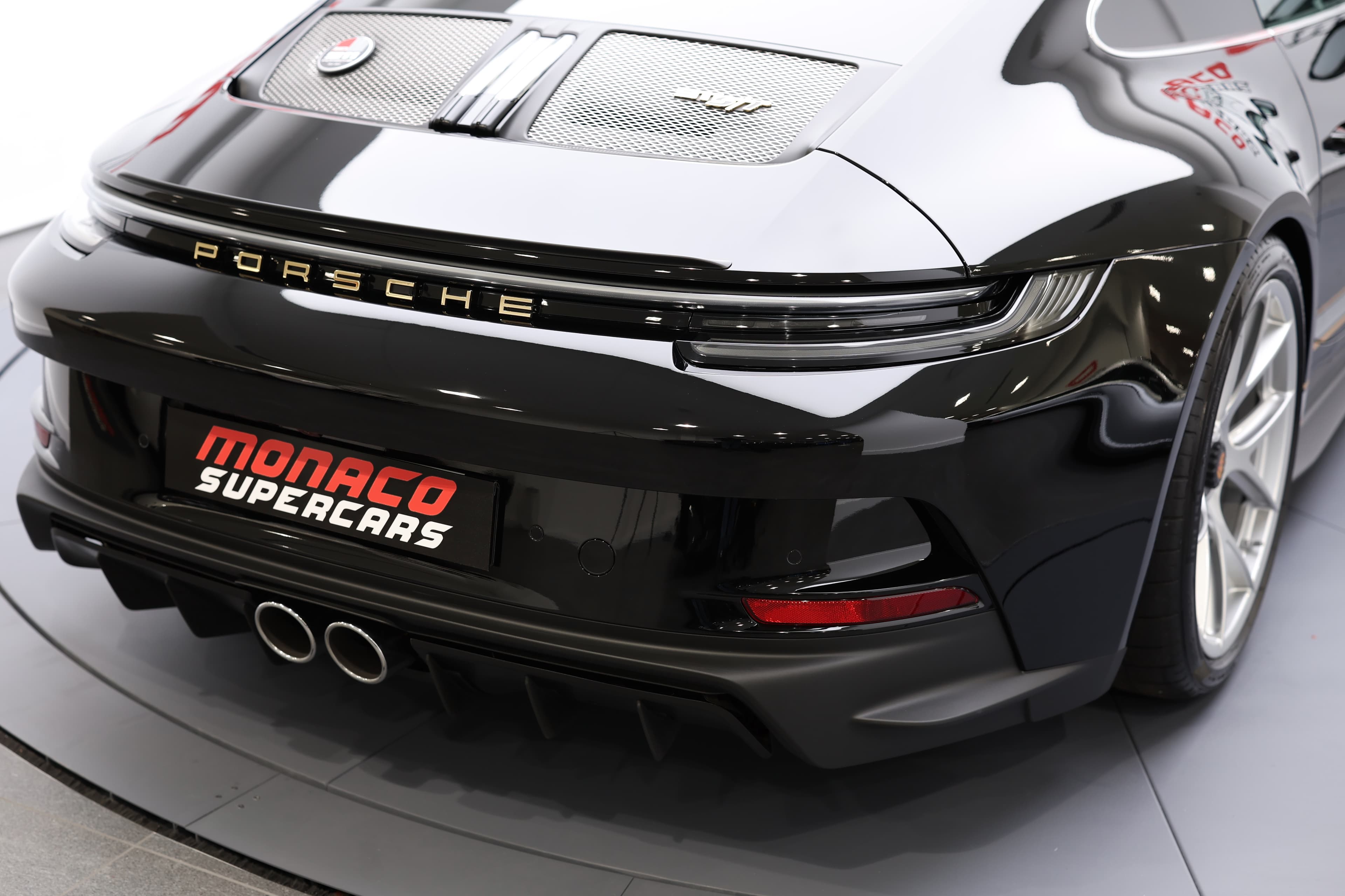 Vue arrière de la Porsche 911, mettant en avant le design élégant et moderne du véhicule. Le logo "PORSCHE" en relief et les sorties d'échappement doubles ajoutent une touche de sportivité, tandis que le badge "Monaco Supercars" souligne l'exclusivité et le prestige de cette voiture de performance. Ce modèle incarne l'alliance parfaite entre sophistication et puissance.
